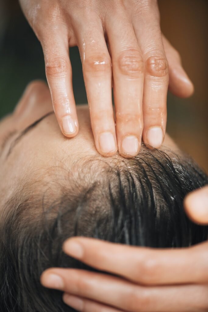Hands applying a treatment to the scalp, representing hair and scalp care.